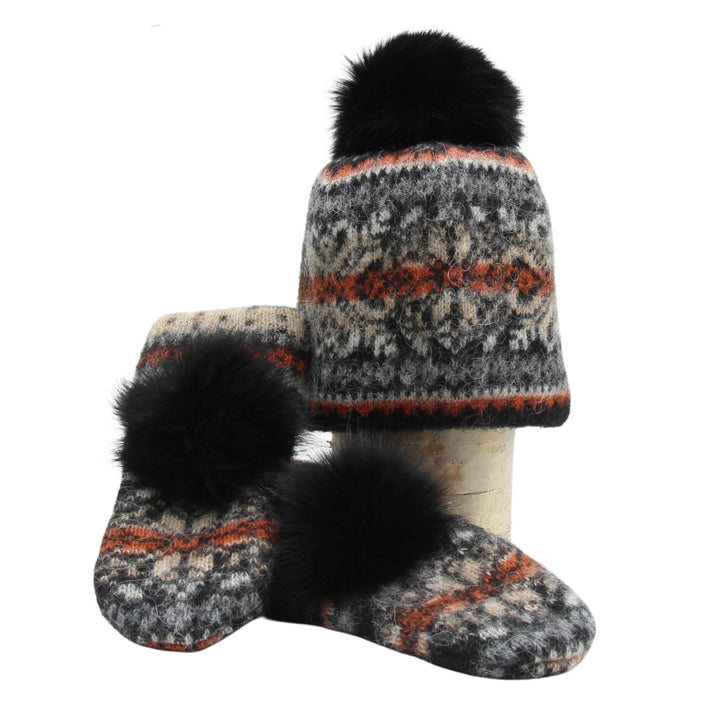 Mitaines et tuque en laine islandaises noires,oranges et jaunes avec un pompom noir déposées sur une buche