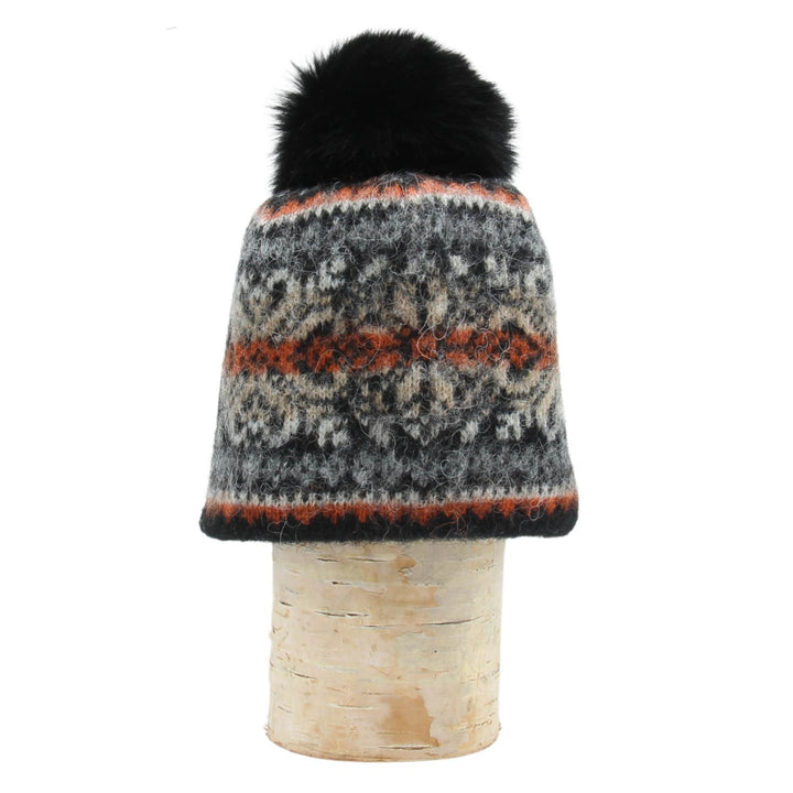 Tuque en laine islandaise grise,noire, orange avec un pompom noir déposée sur une buche
