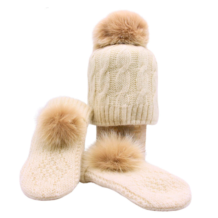 Tuque et mitaines en laine blanche avec pompom en fourrure de renard sur une bûche par Fourrures Audet