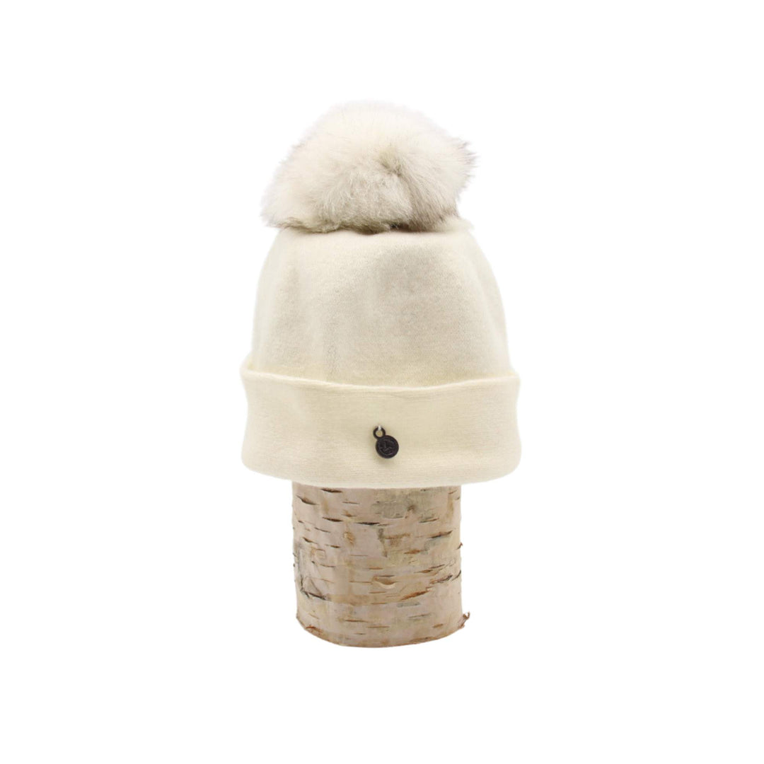 Tuque Odetta blanche par Canadian hat avec un pompom blanc sur le dessus déposée sur une bûche vue de côté