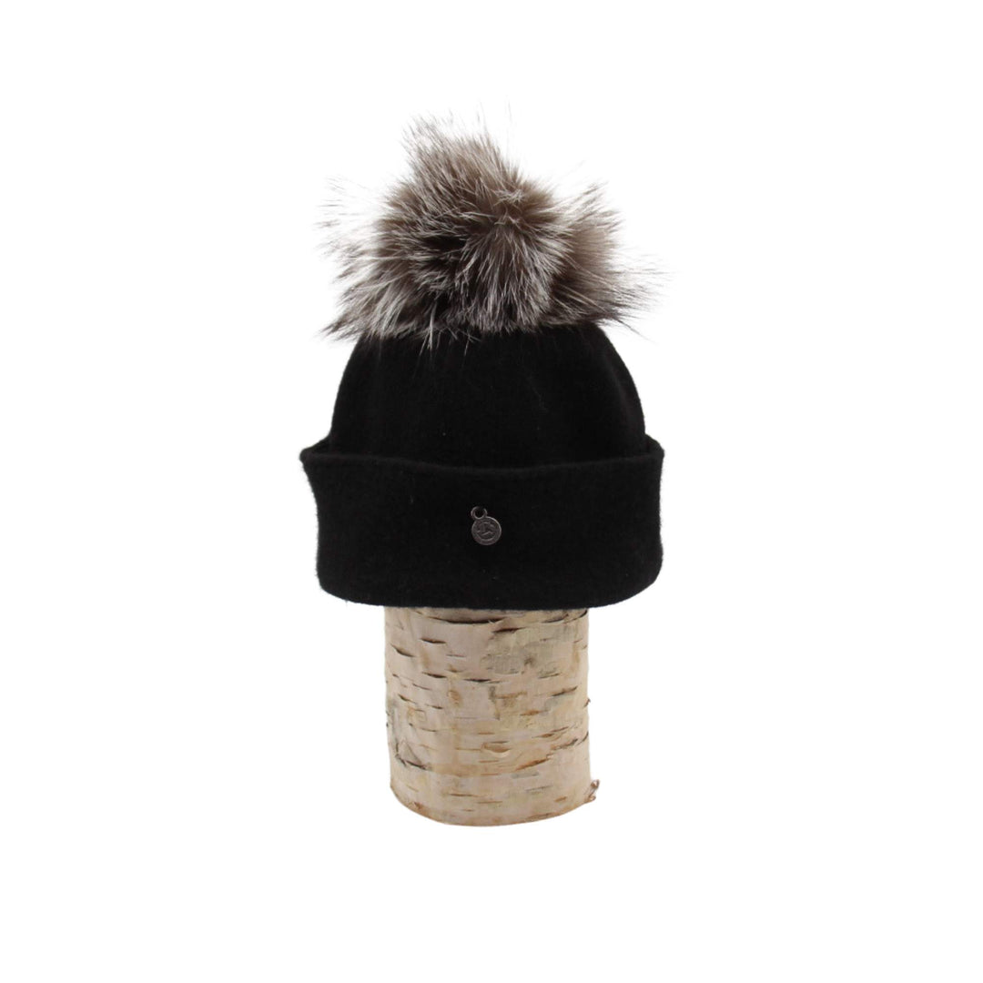 Tuque Odetta noire par Canadian hat avec un pompom gris sur le dessus déposée sur une bûche vue de côté