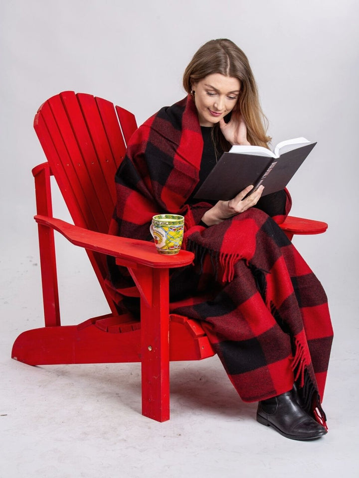 Lourde couverture tartan Rob Roy MacGregor rouge et noire enveloppant une femme lisant un livre sur une chaise rouge avec une tasse jaune