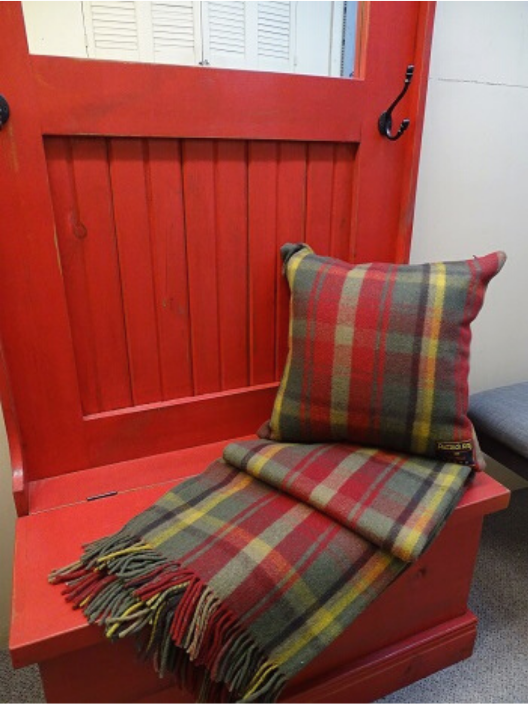 Lourde couverture tartan Canadian Dark Maple verte et rouge avec fines lignes jaunes et franche déposée sous un coussin Tartan assorti sur le devant d'une porte rouge
