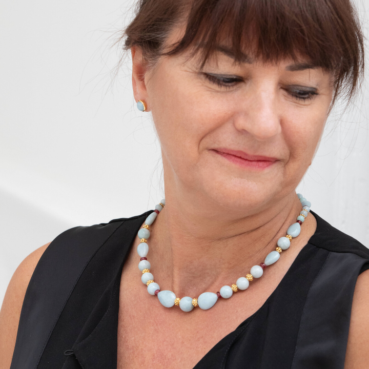 Femme portant une boucle d'oreille ronde de couleur bleue pâle avec un collier assortit de pierres