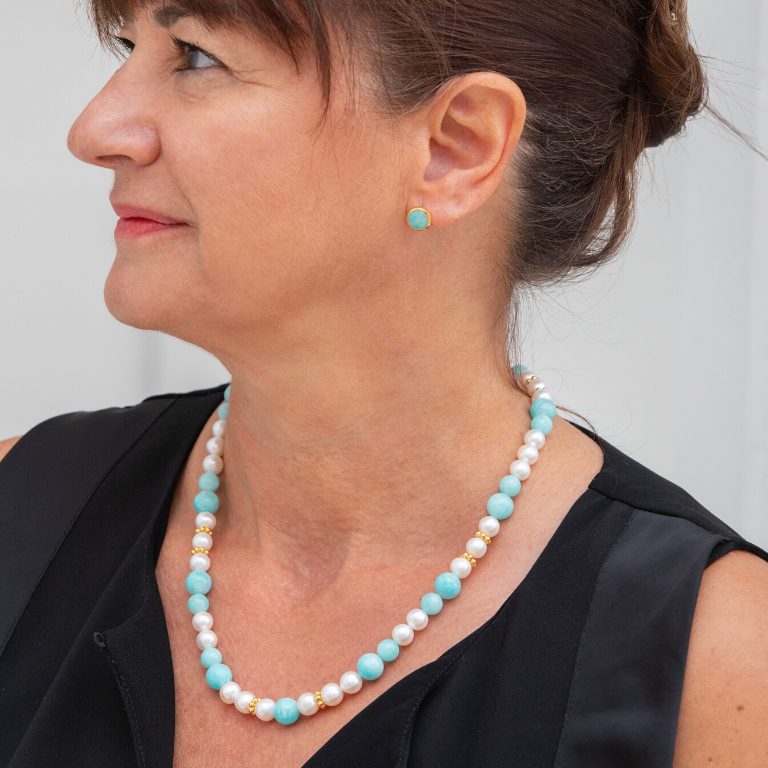 Femme portant une boucle d'oreille turquoise avec un collier assortit de pierres