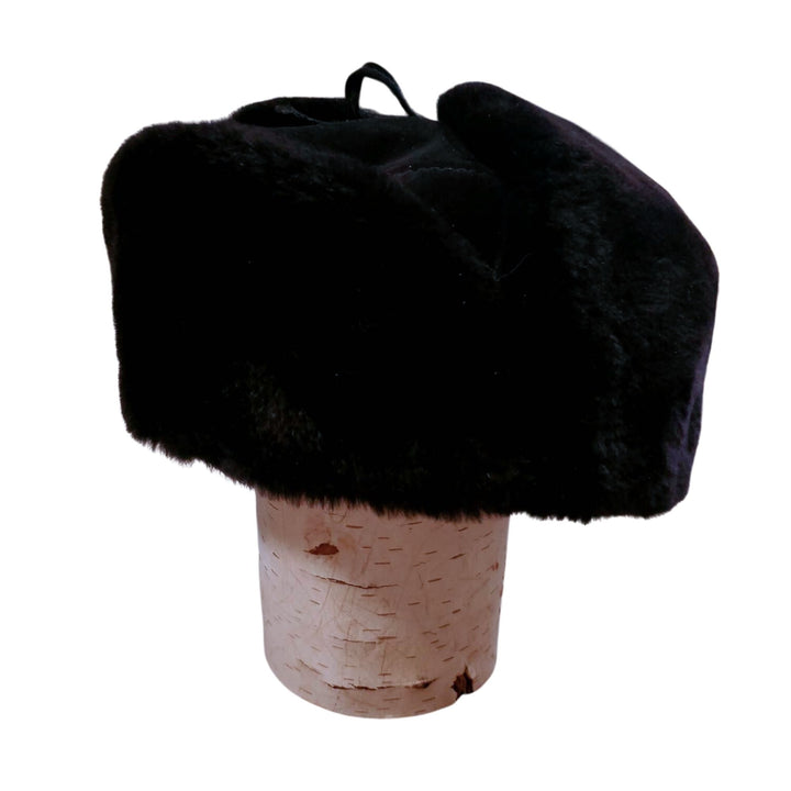 Chapeau d'hiver en castor rasé noir avec oreilles attachées sur le dessus sur une buche