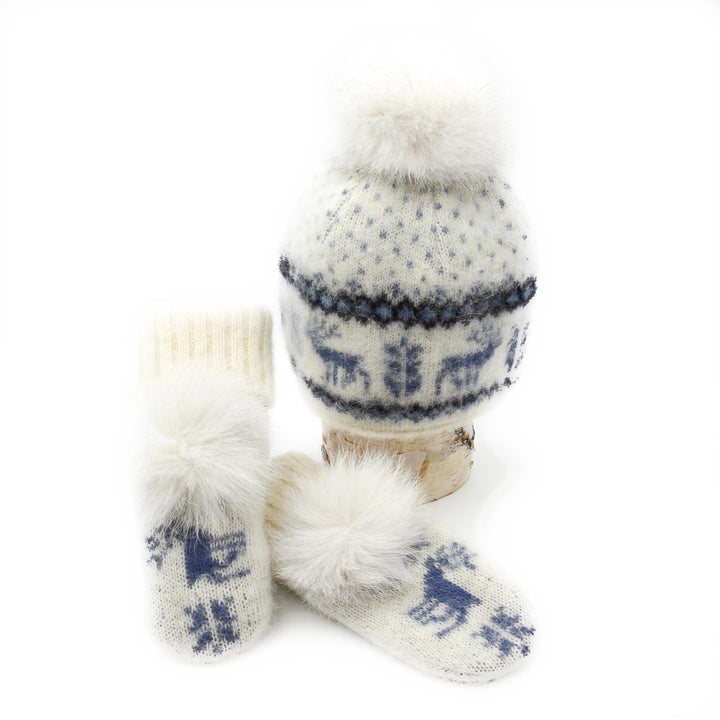 Tuque et mitaines en laine islandaise blanches et bleues avec motif d'orignaux et pompom blanc déposées sur une buche