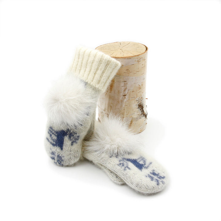 Mitaines en laine islandaises blanches et bleues avec pompoms blanc sur le dessus déposées contre une buche