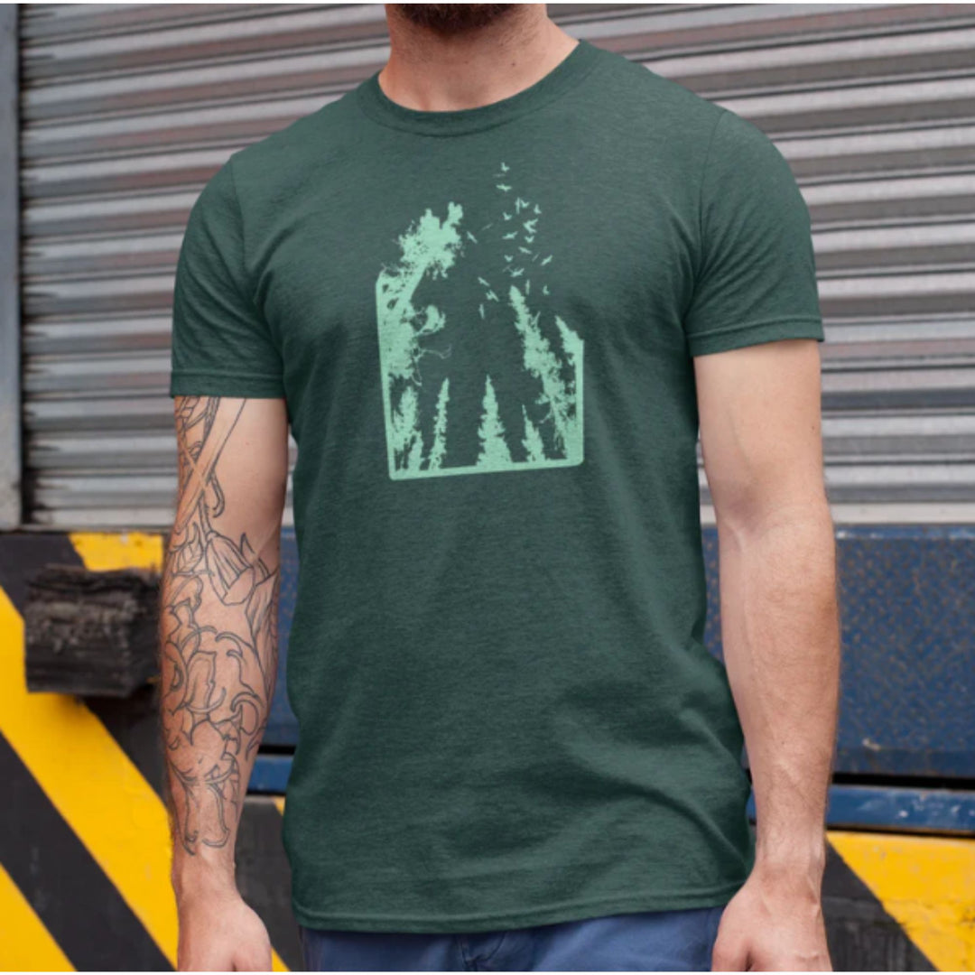 Homme portant un t-shirt KM54 vert avec une forêt et un ciel imprimé