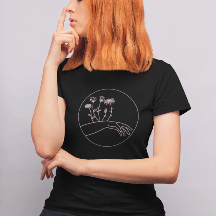 Femme aux cheveux roux portant un t-shirt noir avec une main et des fleurs roses d'imprimées