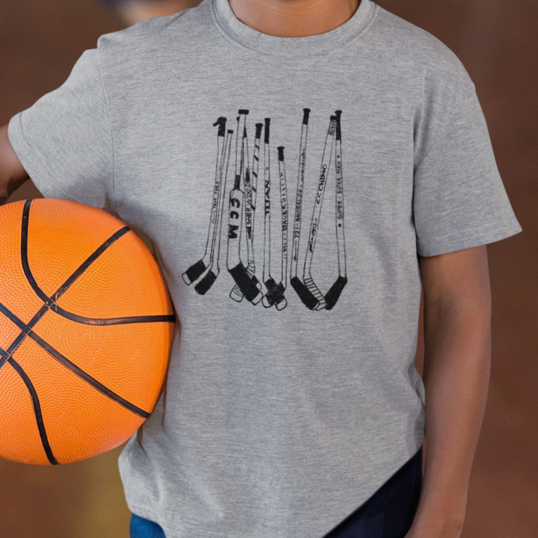 Enfant tenant un ballon de basket portant un t-shirt KM54 gris athlétique avec un motif de bâtons de hockey noirs
