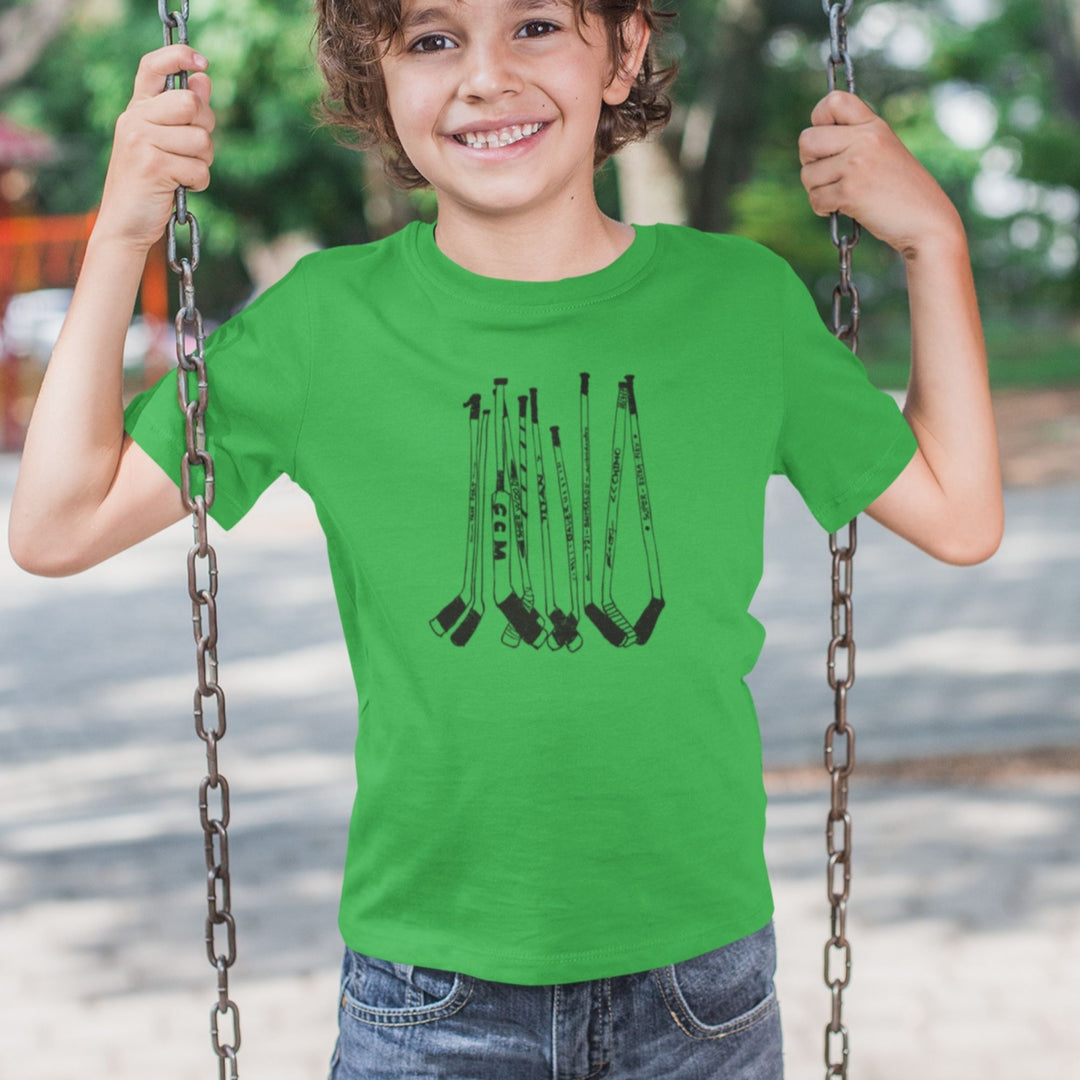 Enfant sur une balançcoire portant un t-shirt KM54 vert kelly avec un motif de bâtons de hockey noirs