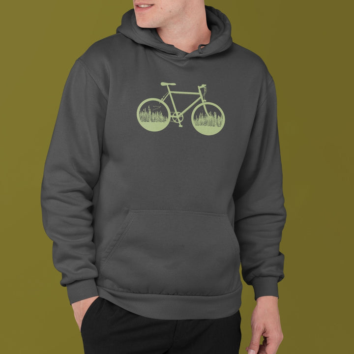 homme qui porte un coton ouaté charcoal avec capuchon sur fond vert. Le coton ouaté a une illustration verte d'un vélo avec deux roues remplies d'arbres et de conifères.